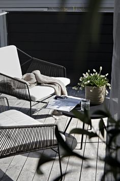 two chairs and a table on a wooden deck with flowers in the potted plant