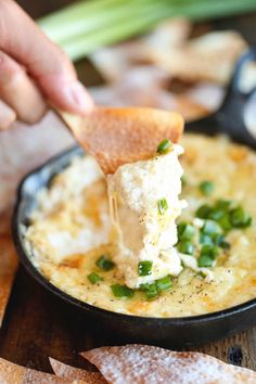 a person dipping some food into a black bowl with green onions and cheese on top