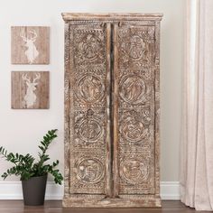 an old wooden armoire next to a potted plant and pictures on the wall