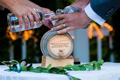 two people are holding wine glasses over a wooden barrel on a table with greenery