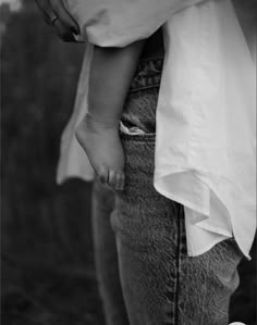 a black and white photo of a person holding a baby's hand in their pocket