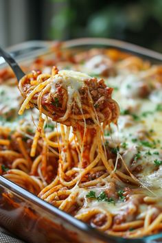 a fork full of spaghetti being lifted from a casserole dish with meat and cheese