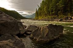 a river with rocks in the middle and trees on both sides, surrounded by mountains