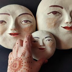 three white masks with faces painted on them being held by a person's hand