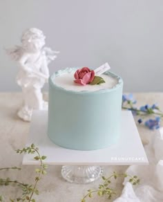 a small blue cake with a pink flower on top and angel figurine in the background