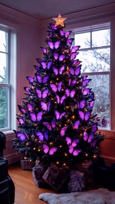 a purple christmas tree with lots of butterflies on it's top and lights around the base