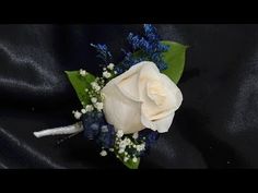 a white rose and baby's breath boutonniere on a black satin background