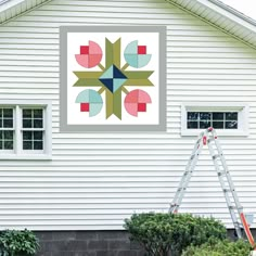 a white house with a large quilt hanging on the wall and a ladder in front of it