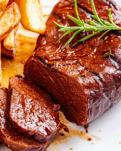 a piece of meat and some french fries on a white plate with rosemary garnish