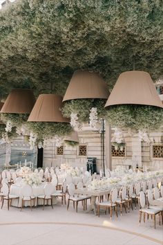 an outdoor wedding setup with white flowers and greenery on the ceiling, surrounded by tall hanging chandeliers