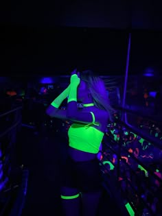 a woman in neon green and black clothing standing next to a railing at night time