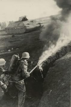 black and white photo of two men in uniform spraying water from a tank while another man watches