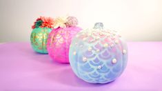 three different colored glass pumpkins sitting on top of a pink tableclothed surface