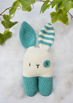 a crocheted stuffed animal sitting on top of snow next to a plant with green leaves