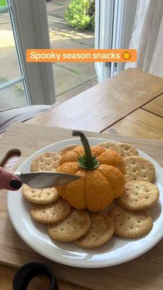 a white plate topped with crackers next to a knife and pumpkin on top of it