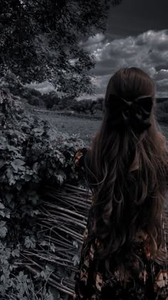 a woman with long hair standing next to a wooden bench under a dark cloudy sky