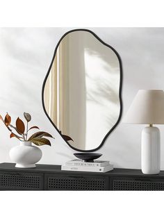 a mirror sitting on top of a black dresser next to a white vase and lamp