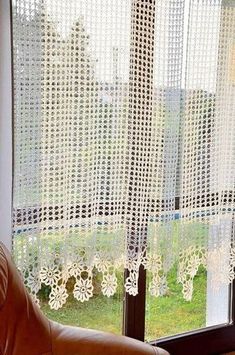 a chair sitting in front of a window next to a brown leather couch and white curtains