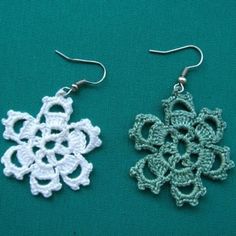 two crocheted earrings are sitting on a green surface, one is white and the other is blue