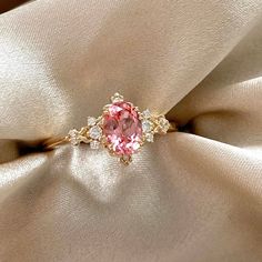 a pink diamond ring sitting on top of a white satin material with gold trimming