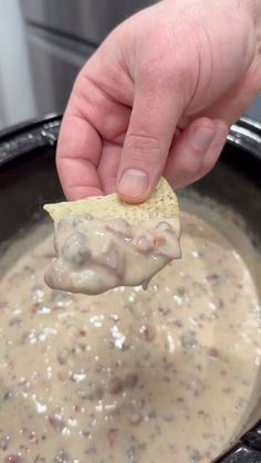 a hand holding a tortilla chip over a bowl of dip and cheese sauce