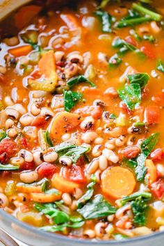 a pot filled with beans and vegetables on top of a wooden table next to utensils