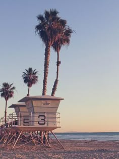 a lifeguard tower sitting on top of a sandy beach next to the ocean with palm trees