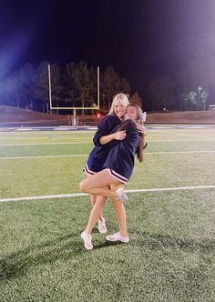 two girls hugging each other on a soccer field at night with lights in the background