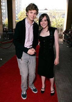 two people standing on a red carpet in front of a building and posing for the camera