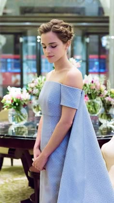 a woman in a blue dress standing next to a table with flowers and vases on it