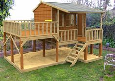 a wooden play house with stairs to the second floor and a deck on one side