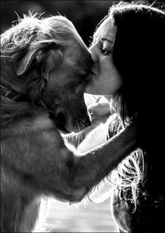 a woman kissing a dog with her face close to it's mouth in black and white