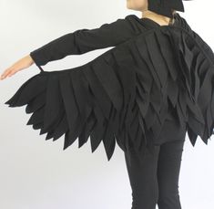 a woman wearing a black hat and jacket with large wings on her back, standing in front of a white background