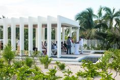 a group of people standing on top of a white gazebo next to palm trees