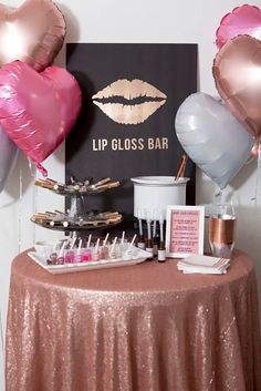 a table topped with lots of pink and silver heart shaped balloons next to a sign that says lip gloss bar