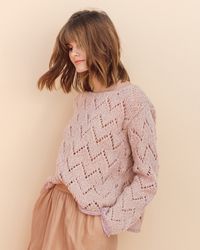 a woman standing in front of a white wall wearing a pink sweater and tan skirt