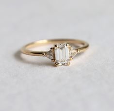 a gold ring with an emerald stone and two diamonds on the side, sitting on a white surface