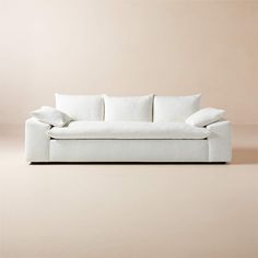 a white couch sitting on top of a floor next to a beige wall with pillows