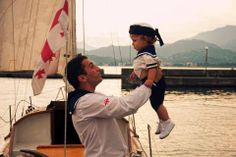 a man holding a small child on his shoulders while standing next to a sailboat