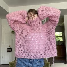 a woman wearing a pink knitted sweater covering her face and hands behind her head