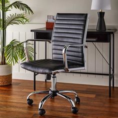 an office chair sitting on top of a hard wood floor next to a potted plant