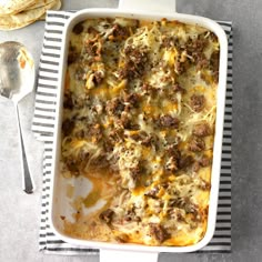 a casserole dish with meat and cheese in it on a striped napkin next to a spoon