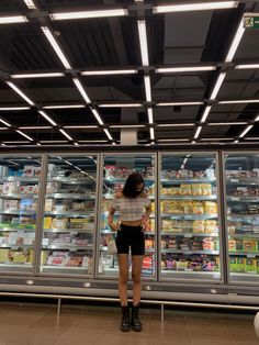 a woman standing in front of a display case filled with food and drink items at a grocery store