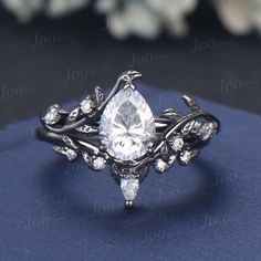 a white gold ring with a pear shaped cut diamond surrounded by leaves and diamonds, on a blue background