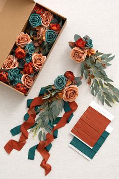 an open box with paper flowers and ribbon on it, next to some other items