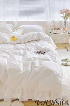 an unmade bed with white sheets and ruffled bedspread in front of a window