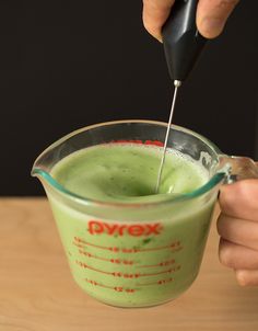 a person is mixing something in a measuring cup with a black spoon and green liquid