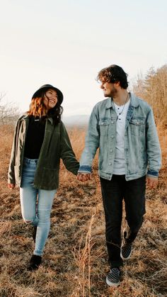 a young man and woman holding hands walking through the grass together in an open field