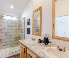 a bathroom with two sinks, a shower and a large mirror on the wall above it