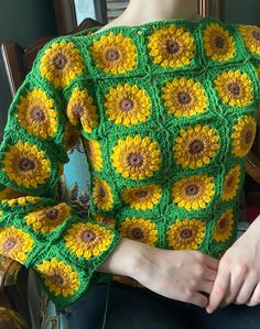 a woman sitting in a chair wearing a green and yellow crochet top with sunflowers on it